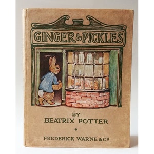 May include: A vintage book cover with a brown background and a green illustration of a rabbit entering a shop called "Ginger & Pickles". The text "By Beatrix Potter" and "Frederick Warne & Co." are printed below the illustration.