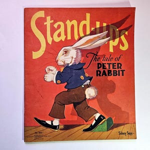 May include: Vintage "Stand-ups" book cover featuring an illustration of Peter Rabbit in a blue jacket and brown pants. The title "The tale of PETER RABBIT" is displayed on a red background with yellow text.