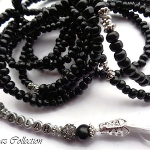 May include: Black beaded prayer beads with a silver charm and a white tassel. The beads are strung on a silver cord and the charm is a small, round pendant with the word "Allah" inscribed on it.