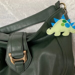 May include: A dark green leather handbag with a gold buckle and a light green felt dinosaur keychain with blue spikes and green and blue spots.