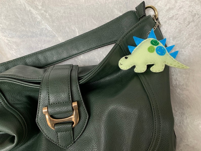 May include: A dark green leather handbag with a gold buckle and a light green felt dinosaur keychain with blue spikes and green and blue spots.