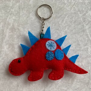 May include: Red felt dinosaur keychain with blue felt spikes and blue and silver buttons.