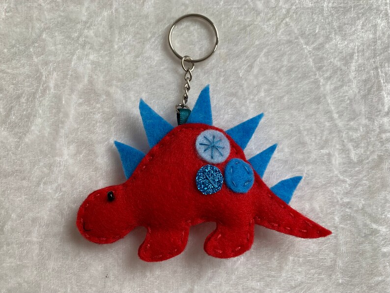 May include: Red felt dinosaur keychain with blue felt spikes and blue and silver buttons.
