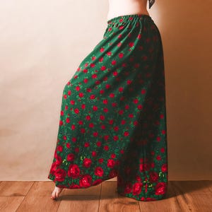 Könnte beinhalten: Grüne weite Hose mit einem sich wiederholenden Muster aus roten Rosen. Die Hose hat einen elastischen Bund und einen floralen Saum. Der Stoff ist dunkelgrün.