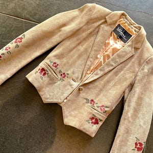 Puede incluir: Una chaqueta de ante beige con bordados florales. La chaqueta tiene un cierre de botón único y una etiqueta "Wilson's of California".