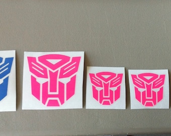 May include: Five vinyl stickers featuring the Autobot symbol in different sizes. The stickers are blue and pink.