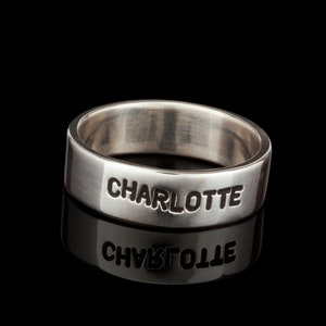 Puede incluir: Un anillo de plata con el nombre "CHARLOTTE" grabado.