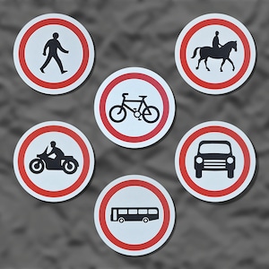 Könnte beinhalten: Eine Sammlung runder Verkehrsschilder mit roten Rändern und weißen Hintergründen. Die Schilder zeigen verschiedene Verkehrsmittel, darunter einen Fußgänger, ein Fahrrad, ein Motorrad, ein Auto, einen Bus und eine Person auf einem Pferd. Die Symbole sind schwarz.