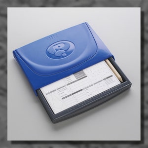 May include: A blue plastic case with a question mark logo on the front. The case is open, revealing a white paper with a grid and a pencil. The paper has the words "Answer Grid" and "Answer Sheet" printed on it.