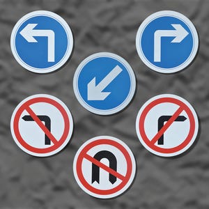 May include: Six circular road signs with white arrows on blue backgrounds indicating direction, and red-ringed signs with black turn symbols, indicating restrictions. The signs are on a grey background. Metric measurements are not applicable.