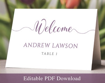 Puede incluir: Una tarjeta de mesa blanca y plegada con la palabra "Welcome" en fuente cursiva y el nombre "ANDREW LAWSON" impreso debajo. También es visible el texto "TABLE 1". La parte inferior de la tarjeta dice "Editable PDF Download" en una pancarta púrpura.