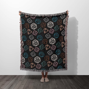 May include: A black woven throw blanket featuring a repeating pattern of colourful dice. The dice are outlined in white and have different numbers on each side.