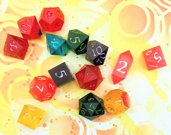 May include: A collection of 12-sided dice in various colors, including red, green, blue, yellow, and black. The dice are scattered on a yellow and orange background with a circular pattern.