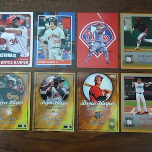 May include: A collection of baseball cards featuring Bryce Harper. The cards display Harper in various team uniforms, including the Nationals, Phillies, and minor league teams. The cards have different designs and years, with text such as "Rookie Phenoms" and team logos.