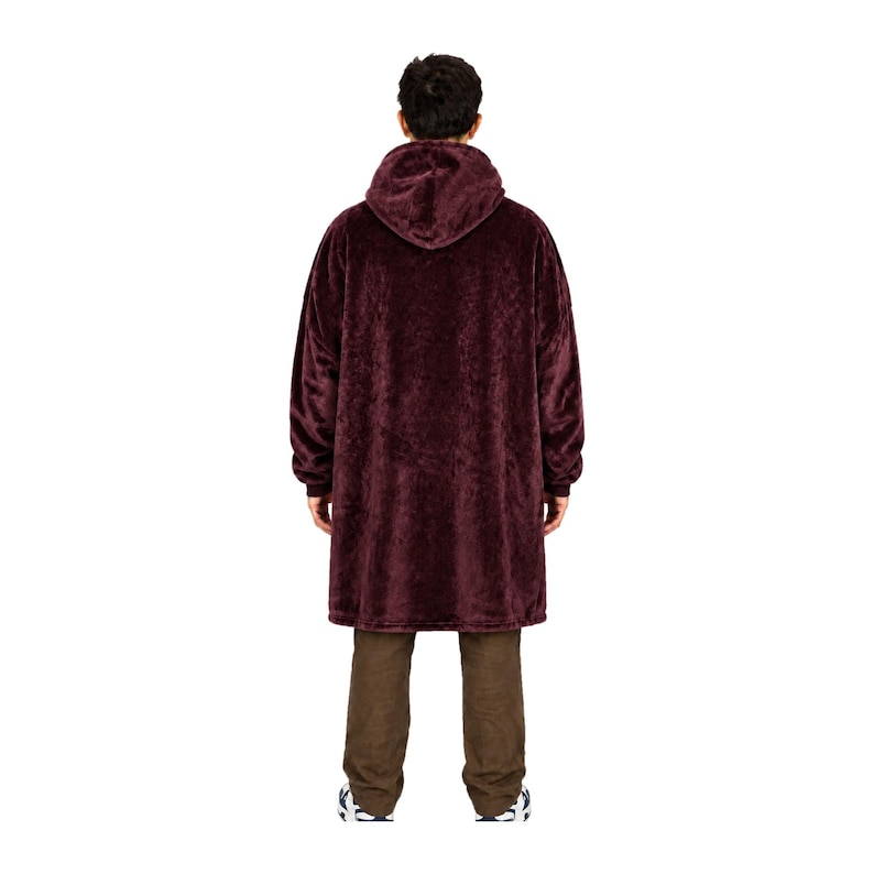 May include: A deep burgundy oversized hooded sweatshirt made of a plush, fuzzy material. The garment features long sleeves with ribbed cuffs, a large hood, and a loose, knee-length fit that hangs straight down, paired with plain brown trousers.