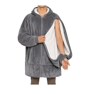 May include: A charcoal gray zip-up hoodie blanket featuring a plush white sherpa fleece lining. The garment includes a hood, long sleeves with ribbed cuffs, and a front zipper closure. The side panel is partially open, revealing the white interior.