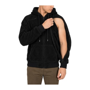 May include: A black zip-up hoodie made of a textured fleece material. The garment features a hood with black drawstrings, ribbed cuffs, and a full-length front zipper. The right sleeve is partially detached, revealing the arm underneath.