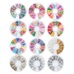 Puede incluir: Doce recipientes redondos llenos de una variedad de decoraciones coloridas para el arte de las uñas. Cada recipiente presenta un diseño diferente de diamantes de imitación, cuentas y otros adornos.