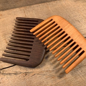 May include: Two wooden combs, one dark brown and one light brown, are lying on a wooden surface. The combs have a rounded shape and are made of natural wood.