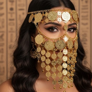 Peut inclure: Coiffe dorée ornée de pièces et de chaînes. Le bijou comprend un bandeau, un voile facial et des boucles d'oreilles pendantes. Les pièces ont un motif en relief. Les cheveux de la femme sont foncés et ondulés.
