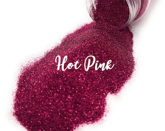 Peut inclure: Un gros plan sur un pot de paillettes rose vif, avec les paillettes qui se répandent sur une surface blanche. Le texte "Hot Pink" est écrit sur les paillettes.