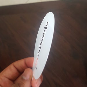 K&ouml;nnte beinhalten: Wei&szlig;e Kunststoffschablone mit einem Design aus einer einzigen Zeile kursiver Schrift. Der Text lautet "Love you more".
