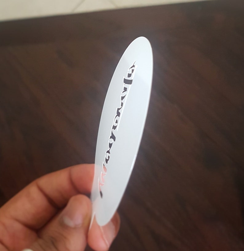 K&ouml;nnte beinhalten: Wei&szlig;e Kunststoffschablone mit einem Design aus einer einzigen Zeile kursiver Schrift. Der Text lautet "Love you more".