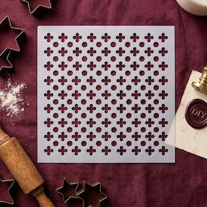 May include: A square, off-white stencil featuring a repeating pattern of circles and four-leaf clovers. Baking tools surround the stencil, including star-shaped cookie cutters, a rolling pin, and a DIY wax seal.