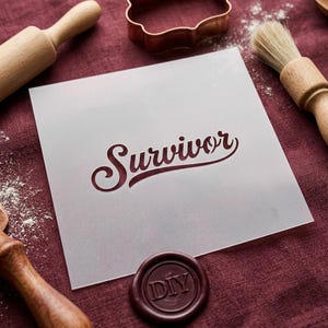 May include: A square, semi-transparent plastic stencil featuring the word Survivor in a cursive script font. The stencil is positioned among baking tools including a wooden rolling pin, a pastry brush, and a copper-colored cookie cutter.