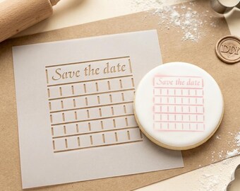 May include: A square translucent stencil featuring the text "Save the date" above a grid of horizontal lines and vertical tick marks, positioned next to a round cookie with the same design airbrushed in pink on a white icing surface.