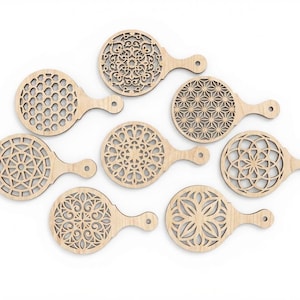 May include: Eight wooden coasters with detailed, laser-cut patterns. Each coaster has a round top and a handle, displaying geometric and floral designs. The natural wood colour gives a neutral appearance. The coasters are approximately 10 cm in diameter.