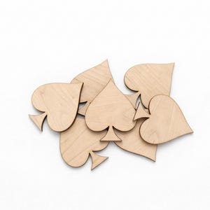 May include: A collection of unfinished wooden playing card suit shapes, including spades and hearts. The shapes are light brown and arranged on a white background. Ideal for crafting or DIY projects.