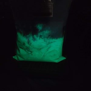 May include: A plastic bag filled with a bright green glowing powder. The powder is in a dark room and is glowing under a black light.