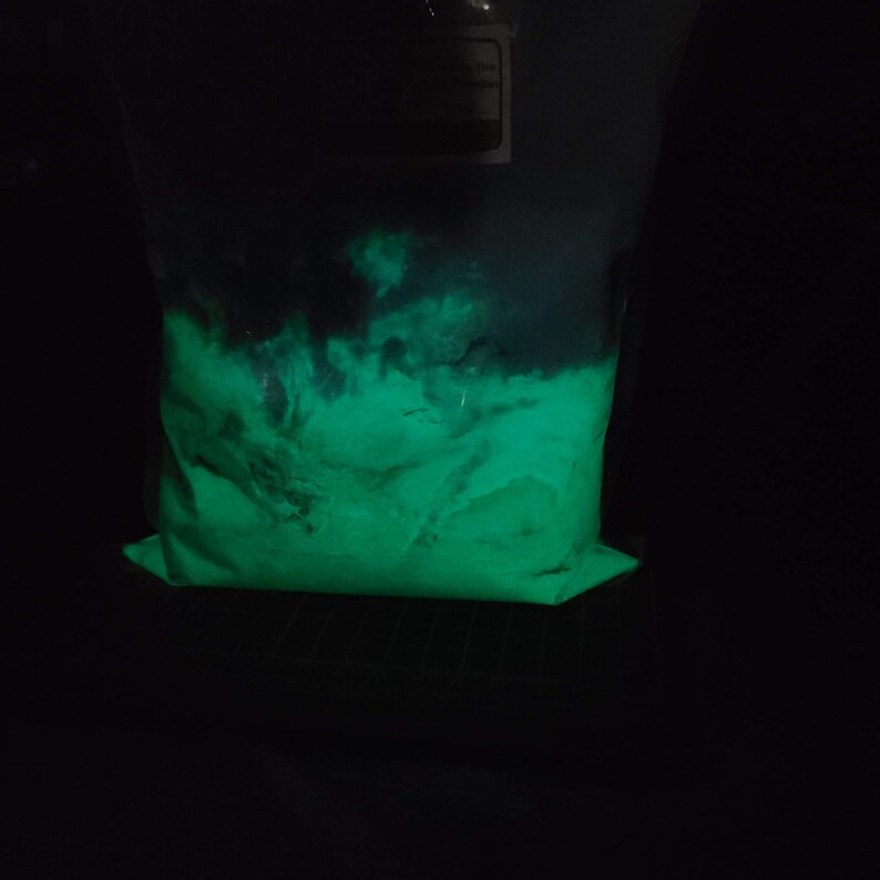 May include: A plastic bag filled with a bright green glowing powder. The powder is in a dark room and is glowing under a black light.