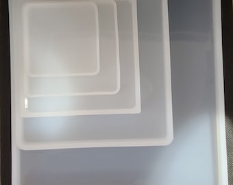 May include: Four white silicone square moulds of different sizes, nested inside each other.