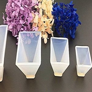 Può includere: Cinque stampi in silicone trasparente a forma di piramidi quadrate, disposti in ordine di grandezza dal più grande al più piccolo. Gli stampi sono su una superficie grigia.
