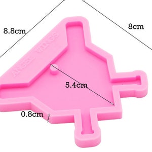 May include: Pink silicone mold shaped like a house with a pointed roof and a chimney. The mold is 8 cm tall, 8.8 cm wide, and 5.4 cm deep. The mold has the text "ANGEL WINGS" on the side.