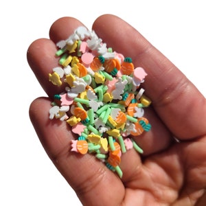 May include: A variety of colourful Easter sprinkles in a hand. The sprinkles are shaped like carrots, bunnies, and eggs. They are in shades of green, orange, yellow, pink, and white.