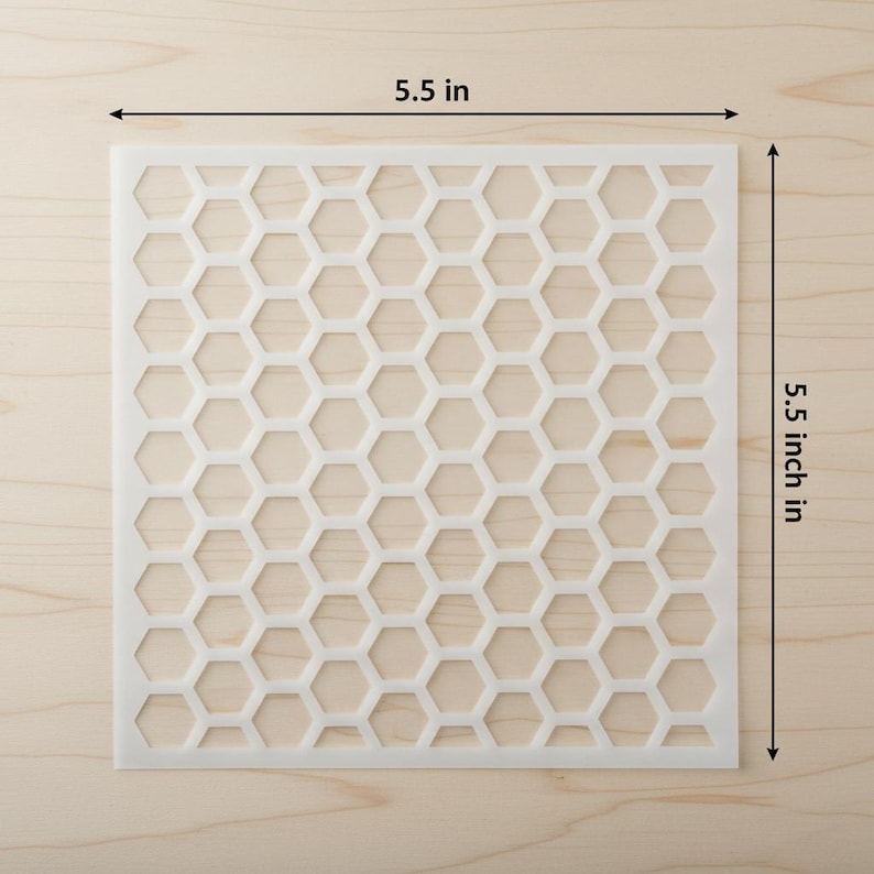 May include: A square, off-white stencil with a honeycomb pattern. The stencil measures 5.5 inches (14 cm) on each side. The design features a repeating pattern of hexagonal shapes, perfect for crafts and DIY projects.