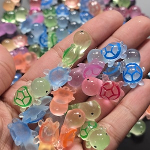 May include: A collection of small, colourful, translucent plastic turtle figurines. The turtles are in various shades of blue, green, pink, and orange. Some of the turtles have painted details, such as eyes and shells.