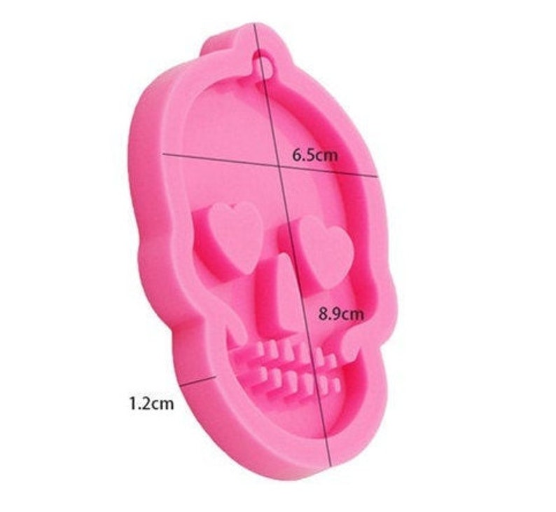 May include: Pink silicone mold shaped like a skull with heart-shaped eyes. The mold measures 6.5 cm wide, 8.9 cm tall, and 1.2 cm thick.