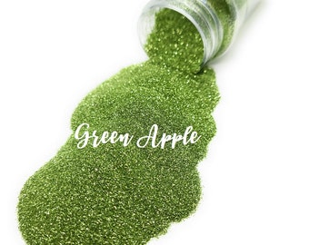 Peut inclure: Un pot en plastique transparent contenant des paillettes vertes. Le pot est renversé et les paillettes se répandent, formant un tas vert. Le texte "Green Apple" est écrit en blanc sur le tas de paillettes.