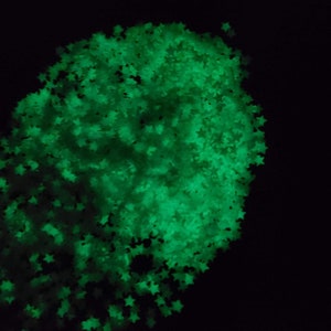 May include: A cluster of glowing green star-shaped confetti against a black background. The stars are densely packed, creating a bright, luminous effect. Ideal for crafts, decorations, or adding a touch of sparkle.