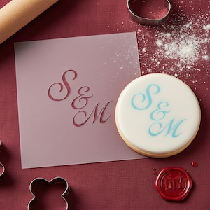 May include: A round cookie with blue "S & M" lettering sits next to a stencil with the same design. A red wax seal with "DIY" is also present. Baking-themed image.