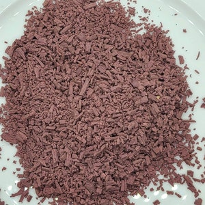 May include: A close-up of a pile of dried, shredded purple hibiscus flowers. The flowers are a deep reddish-purple color and have a slightly textured surface.