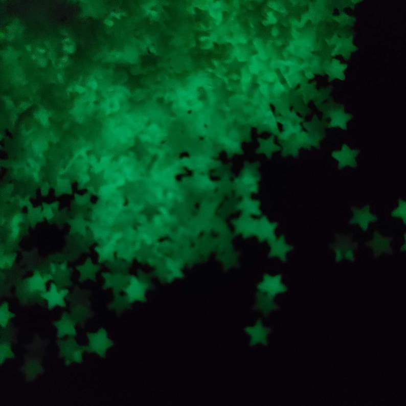 May include: A collection of glowing green star-shaped confetti against a black background. The stars are out of focus, creating a soft, ethereal effect. The image suggests a festive or decorative theme.