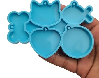 May include: A blue silicone mold with five different shapes for making resin keychains: a bone, a cat, a heart, a circle, and a fish.