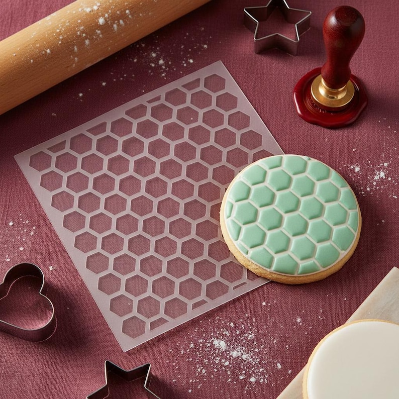 May include: A honeycomb-patterned cookie stencil and a decorated cookie with a green honeycomb design are displayed. Other baking tools include a rolling pin, cookie cutters, and a stamp. The items are arranged on a maroon surface with flour.