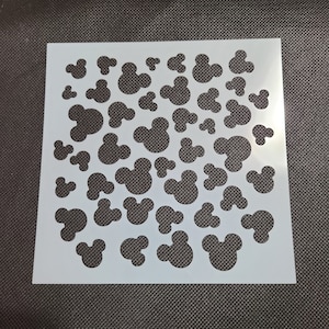 K&ouml;nnte beinhalten: Wei&szlig;e Kunststoffschablone mit einem sich wiederholenden Muster aus Mickey-Maus-K&ouml;pfen in verschiedenen Gr&ouml;&szlig;en.