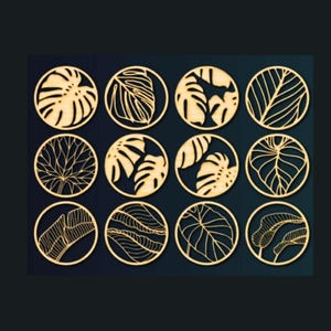 May include: Twelve round wooden coasters with intricate laser-cut designs of tropical leaves in a gold color.